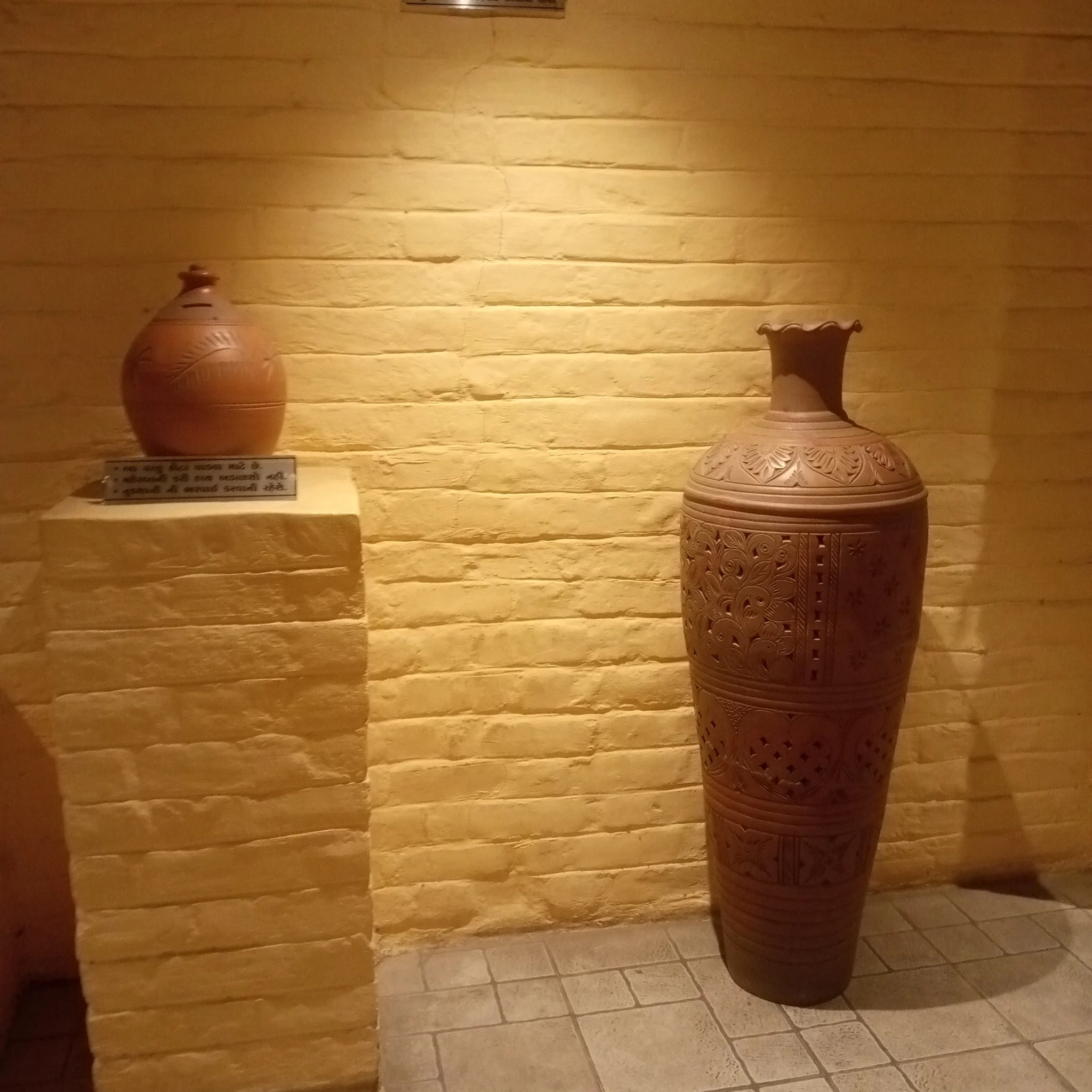 Two carved terracotta pots against a yellow brick wall