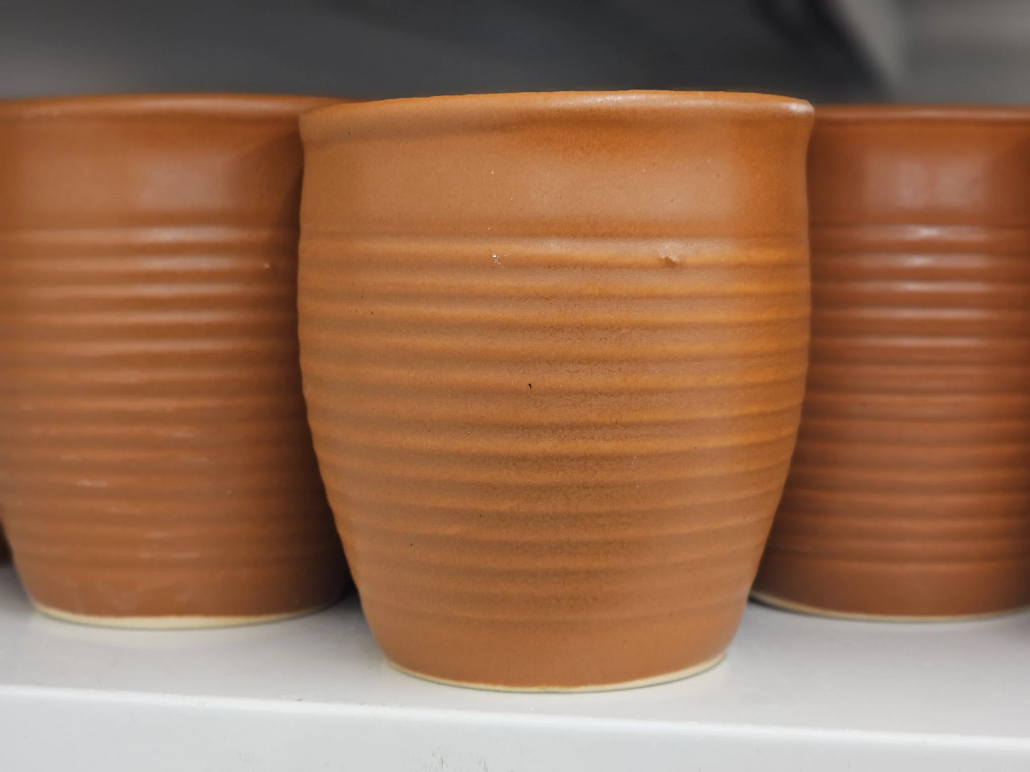 A row of ribbed terracotta cups on a shelf